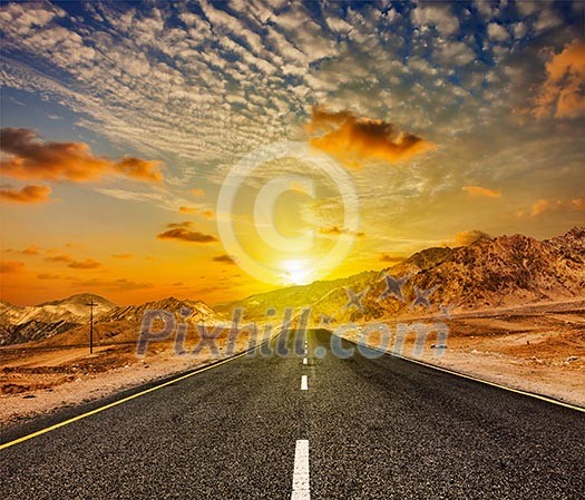 Travel forward concept background - road in Himalayas with mountains and dramatic clouds on sunset. Ladakh, Jammu and Kashmir, India