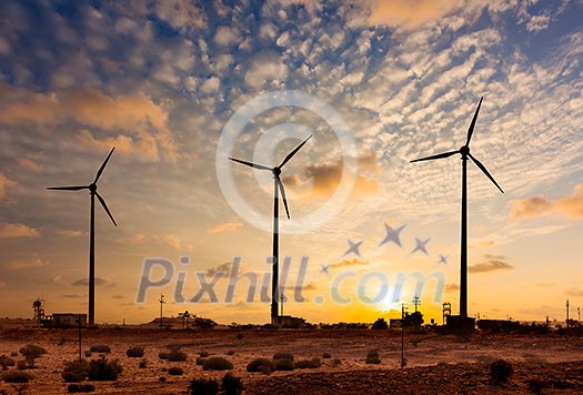 Green renewable energy concept - wind generator turbines sihouettes on sunset