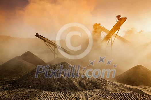 Industrial hell pollution background concept - crusher rock stone crushing machine at open pit mining and processing plant for crushed stone, sand and gravel on sunset