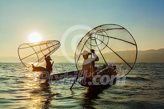 Myanmar travel attraction landmark - two traditional Burmese fishermen at Inle lake, Myanmar famous for their distinctive one legged rowing style on sunrise sunset Myanmar travel attraction landmark - two traditional Burmese fishermen at Inle lake, Myanmar famous for their distinctive one legged rowing style on sunrise sunset