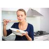 Pretty, young woman cooking a diner in a modern kitchen, tasing the food she made