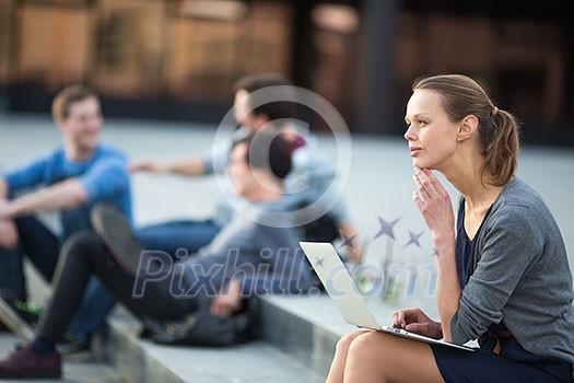 Portrait of a sleek young woman, using laptop computer, being pensive in urban/city context (shallow DOF; color toned image)