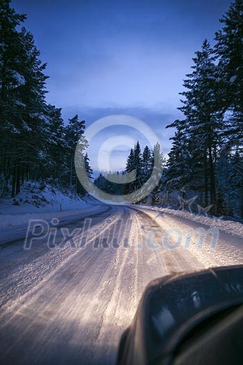Car driving on winter road with headlights lit.