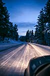 Car driving on winter road with headlights lit.