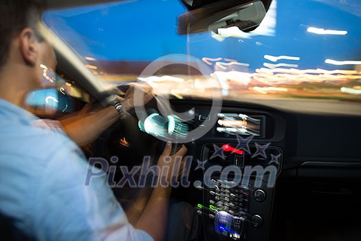 Driving a car at night - young man driving his modern car at night in a city (shallow DOF; color toned image, motion blur technique used to convey speed of the fast driving and drama) Driving a car at night - young man driving his modern car at night in a city (shallow DOF; color toned image, motion blur technique used to convey speed of the fast driving and drama)