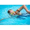 Young girl in goggles and cap swimming crawl stroke style in the blue water pool