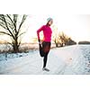 Young woman stretching while running outdoors on a cold winter evening