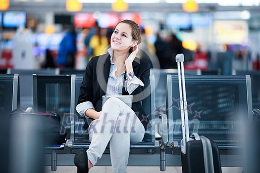 Young female passenger at the airport, using her tablet computer while waiting for her flight (color toned image)