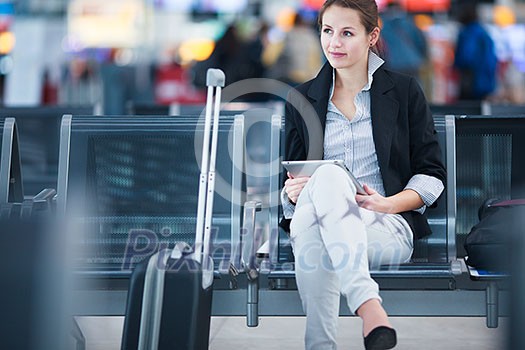 Young female passenger at the airport, using her tablet computer while waiting for her flight (color toned image)