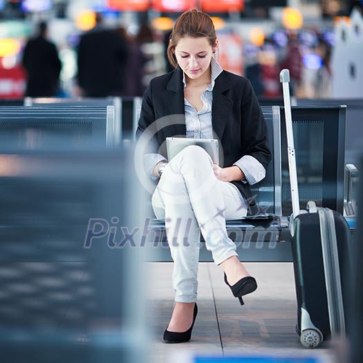 Young female passenger at the airport, using her tablet computer while waiting for her flight (color toned image)