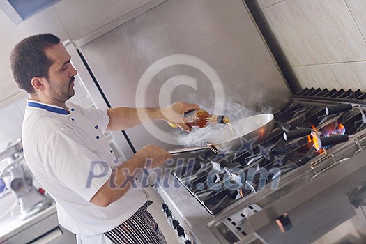 Handsome chef dressed in white uniform decorating pasta salad and seafood fish in modern kitchen