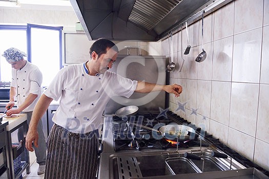 Handsome chef dressed in white uniform decorating pasta salad and seafood fish in modern kitchen