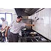 Handsome chef dressed in white uniform decorating pasta salad and seafood fish in modern kitchen