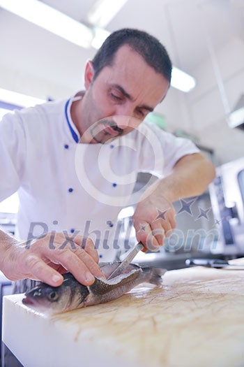 Handsome chef dressed in white uniform decorating pasta salad and seafood fish in modern kitchen