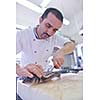 Handsome chef dressed in white uniform decorating pasta salad and seafood fish in modern kitchen