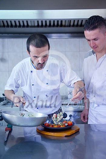 Handsome chef dressed in white uniform decorating pasta salad and seafood fish in modern kitchen Handsome chef dressed in white uniform decorating pasta salad and seafood fish in modern kitchen