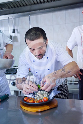 Handsome chef dressed in white uniform decorating pasta salad and seafood fish in modern kitchen