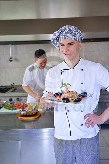 Handsome chef dressed in white uniform decorating pasta salad and seafood fish in modern kitchen Handsome chef dressed in white uniform decorating pasta salad and seafood fish in modern kitchen