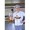 Handsome chef dressed in white uniform decorating pasta salad and seafood fish in modern kitchen