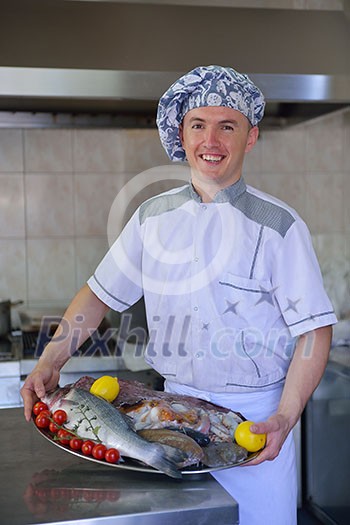 Handsome chef dressed in white uniform decorating pasta salad and seafood fish in modern kitchen Handsome chef dressed in white uniform decorating pasta salad and seafood fish in modern kitchen