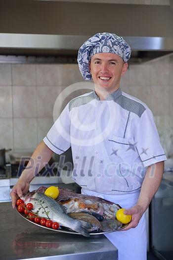 Handsome chef dressed in white uniform decorating pasta salad and seafood fish in modern kitchen