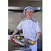 Handsome chef dressed in white uniform decorating pasta salad and seafood fish in modern kitchen