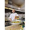 Handsome chef dressed in white uniform decorating pasta salad and seafood fish in modern kitchen