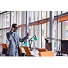Happy smiling successful African American businessman  in a suit in a modern bright office indoors speel on phone