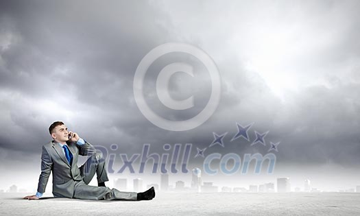 Image of young businessman with mobile phone sitting on floor