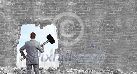 Young businessman with big hammer against wall