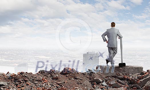 Young businessman with hammer standing on ruins Young businessman with hammer standing on ruins