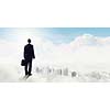 Back view of businessman standing on cloud high in sky