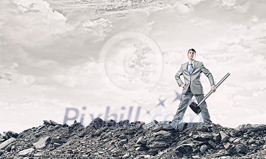 Young businessman with hammer standing on ruins Young businessman with hammer standing on ruins