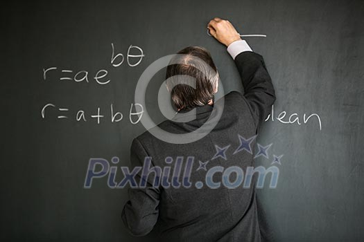 Senior male teacher teaching mathematics, writing on the blackboard