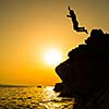 Boy jumping to the sea. Silhouette shot against the sunset sky. Boy jumping off a cliff into the ocean. Summer fun lifestyle.