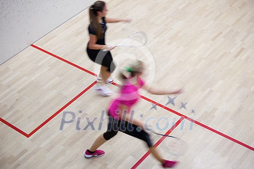 Two female squash players in fast action on a squash court (motion blurred image; color toned image) Two female squash players in fast action on a squash court (motion blurred image; color toned image)