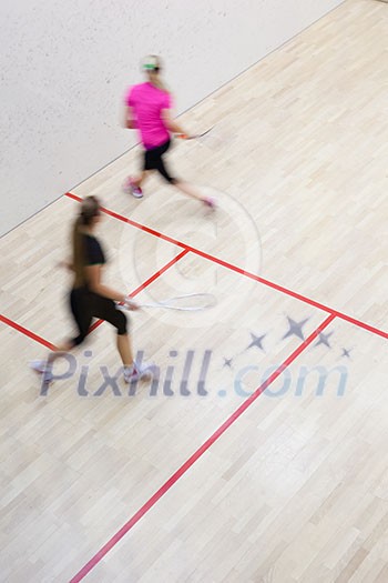 Two female squash players in fast action on a squash court (motion blurred image; color toned image) Two female squash players in fast action on a squash court (motion blurred image; color toned image)