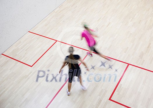 Two female squash players in fast action on a squash court (motion blurred image; color toned image) Two female squash players in fast action on a squash court (motion blurred image; color toned image)