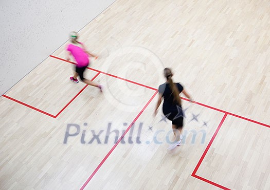 Two female squash players in fast action on a squash court (motion blurred image; color toned image)