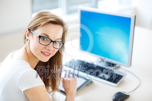 Smiling female student/ businesswoman using her tablet computer and a desktop computer, staying up to date, working, looking at the camera.