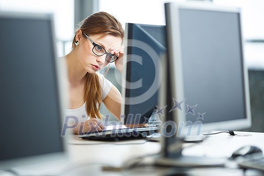 Pretty, female student looking at a desktop computer screen, learning unpleasant news about her exam results. University/office/school concept
