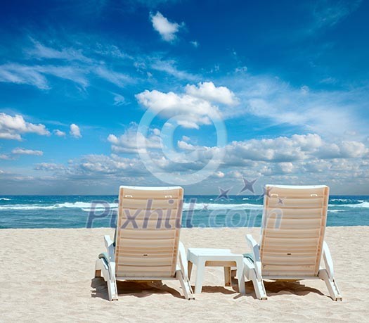 Two sun beach chairs on shore near ocean