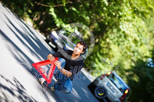 Handsome young man with his car broken down by the roadside, setting the safety triangle