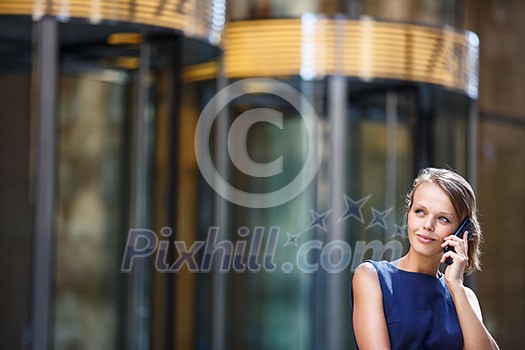 Gorgeous young businesswoman calling on her phone in front of her company's building (shallow DOF; color toned image)