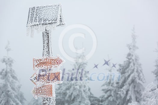 Extreme winter weather - hiking path sign covered with snow brought by strong wind during snowstorm Extreme winter weather - hiking path sign covered with snow brought by strong wind during snowstorm