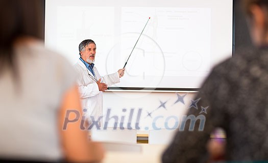 Senior chemistry professor giving a lecture in front of classroom full of students (shallow DOF; color toned image)