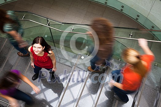 At the university/college - Students rushing up and down a busy stairway - confident pretty young female student looking upwards (color toned image) At the university/college - Students rushing up and down a busy stairway - confident pretty young female student looking upwards (color toned image)