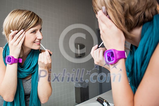 Pretty, young woman applying mascara /eyeshadows in front of a mirror Pretty, young woman applying mascara /eyeshadows in front of a mirror