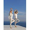 young couple practicing yoga at sunset in modern home terace with ocean and sunset in background