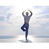 handsome young man practicing yoga on in modern home terace with ocean and sunset in background